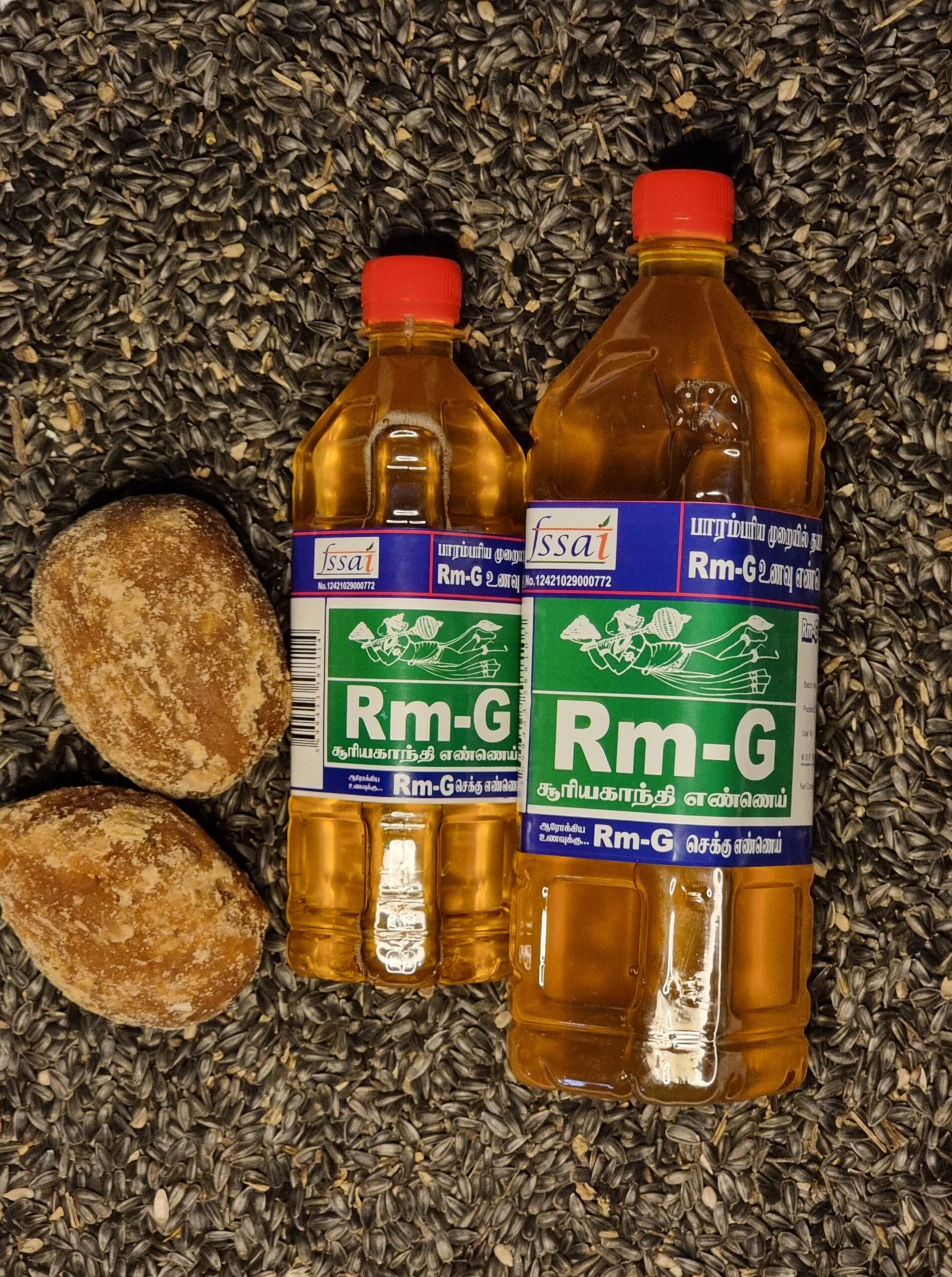 Two bottles of Rm-G unrefined sunflower chekku oil placed on sunflower seeds with jaggery pieces beside them.
